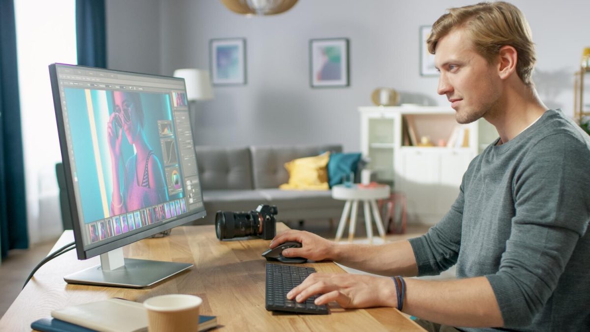 Férfi grafikus számítógépen hirdetéshez retusál egy portrét a monitor előtt ülve